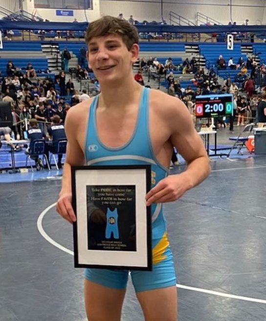 Wrestler Nick Marck, in a light blue singlet, holds a trophy.