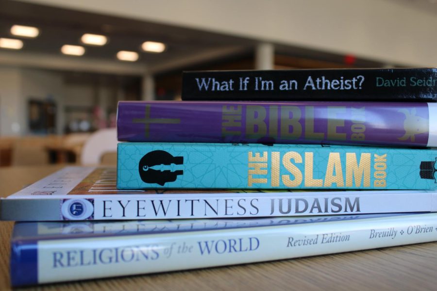 A stack of books about various religions sits on a table,