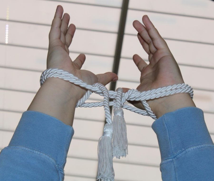 Two hands tied together with a white graduation cord