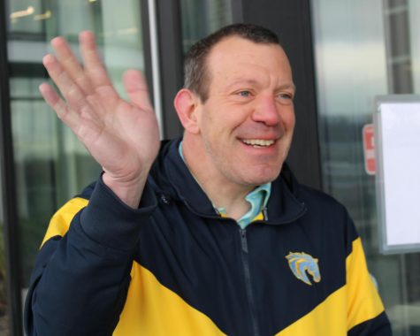 Dr. Ryan Hitchman, wearing a blue and yellow jacket, waves to someone out of frame.