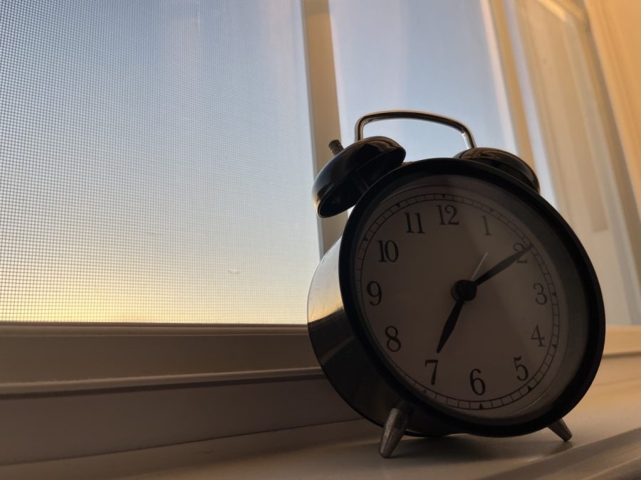 A clock sits by a window, through which the sun is rising.