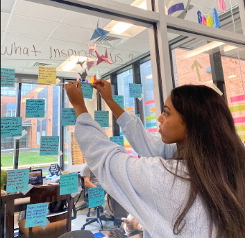 Writing Center member Hasset Mikias makes a note about what inspires her to write and posts it on the window outside the center.  